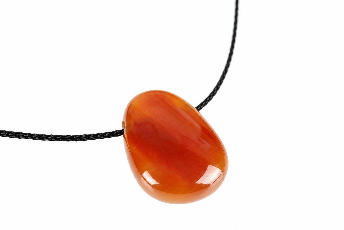 A polished, teardrop-shaped pendant in orange and red tones hangs from a black cord against a white background.