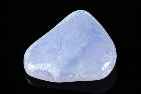 A smooth, polished stone with a pale blue and white cloudy pattern rests on a dark surface.
