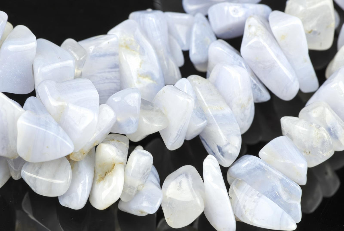 A strand of polished white and pale blue chalcedony chips with subtle banding, arranged on a dark surface.