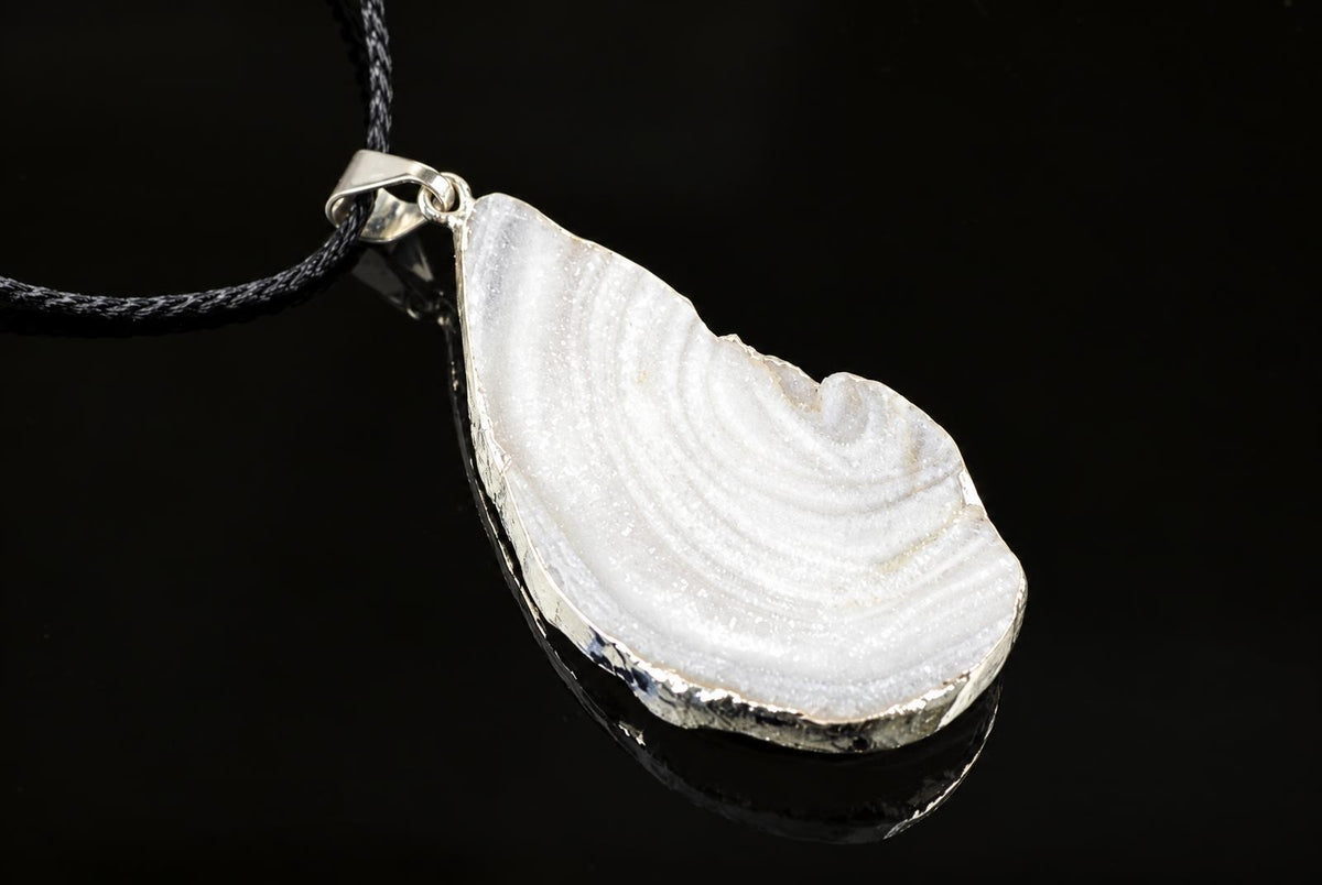 A silver-toned pendant with a white chalcedony stone featuring concentric bands, set in an irregular frame on a black surface.