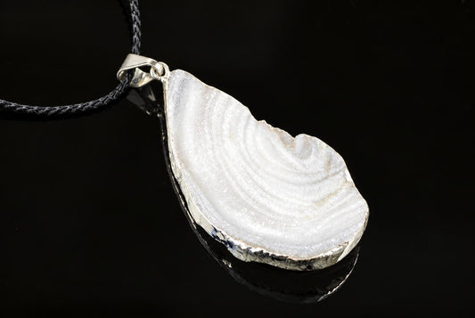 A silver-toned pendant with a white chalcedony stone featuring concentric bands, set in an irregular frame on a black surface.