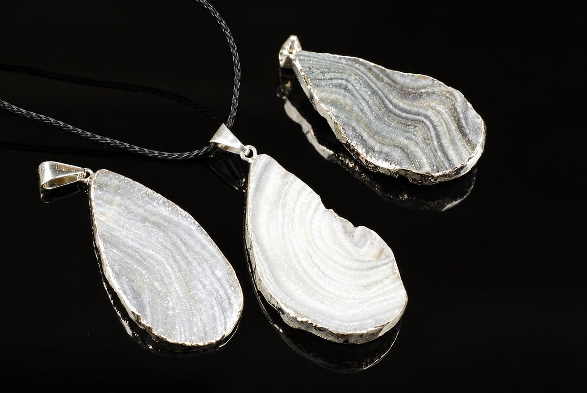 Three teardrop-shaped chalcedony pendants with silver-toned edges and layered patterns on a dark reflective surface.