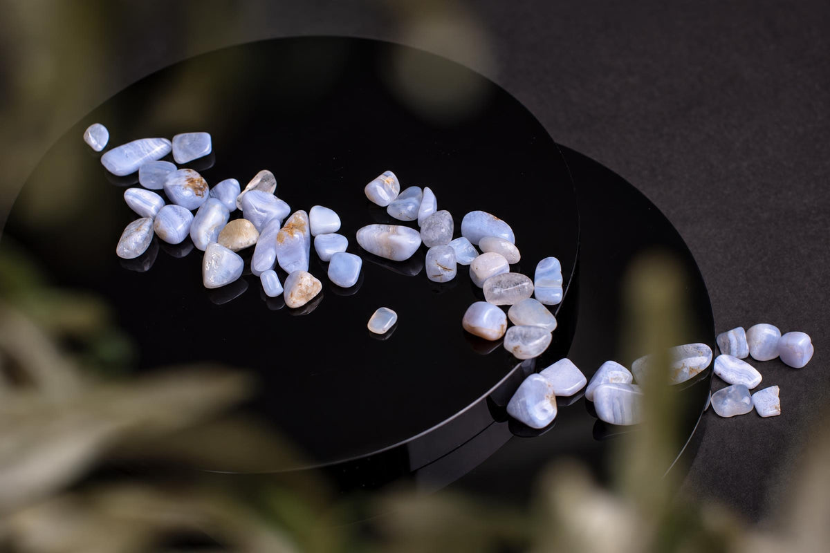 Small, smooth chalcedony stones in pale blue and white with brown spots rest on a glossy black circular surface.