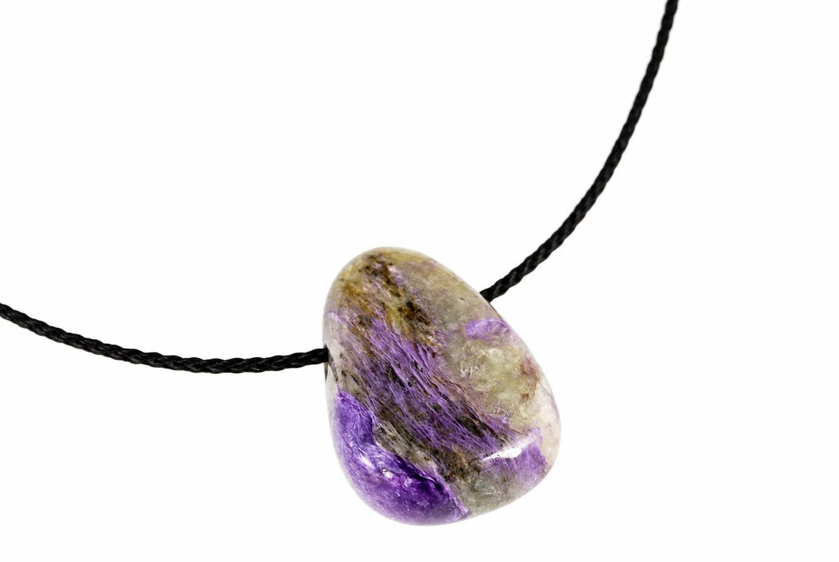 A polished Charoite pendant with purple, green and brown streaks on a black cord against a white background.