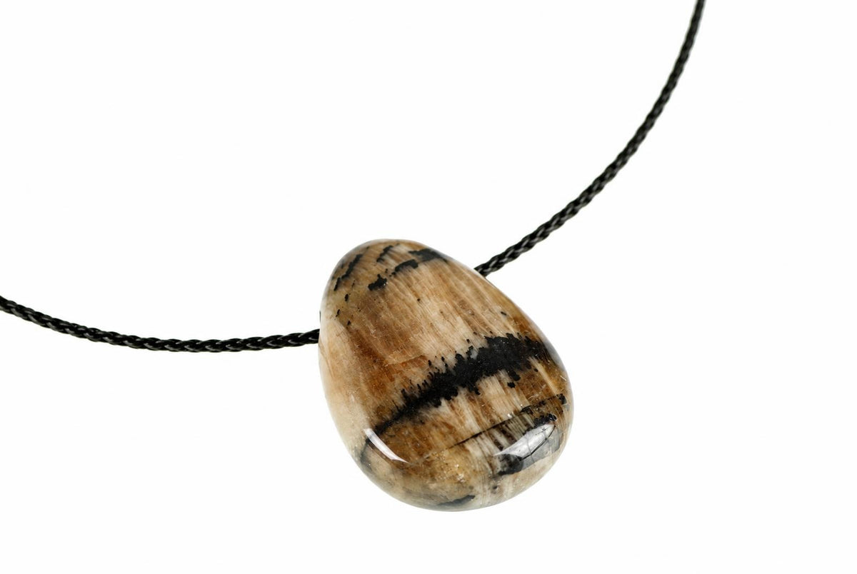 A polished teardrop pendant with brown, black and white stripes hangs on a dark cord against a pale surface.