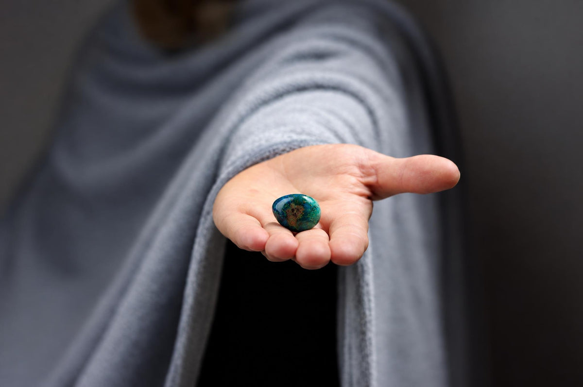 A person in a grey garment holds a polished, oval stone with dark blue and green swirls in their open palm.
