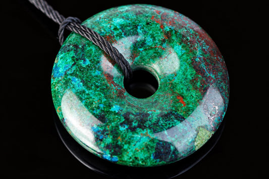 A polished, donut-shaped pendant with green, blue and red mottled patterns on a dark surface.