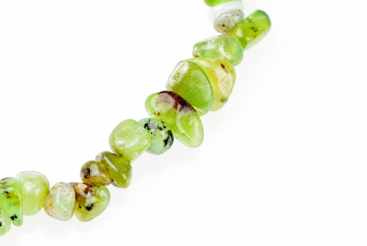 A string of irregular, polished green beads with dark inclusions on a white surface.
