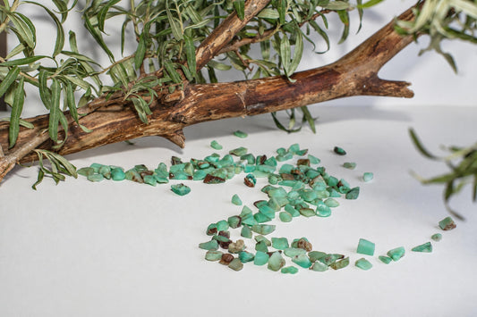Scattered green chrysoprase chips on a white surface, with a branch and leaves in the background.