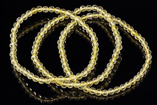 A bracelet of faceted, pale yellow beads arranged in a loop on a dark, reflective surface.