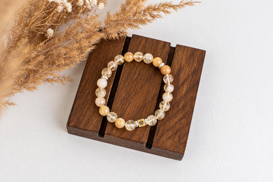 A beaded bracelet with yellow and clear stones, silver spacers, and a gold-toned charm rests on a dark wooden surface.
