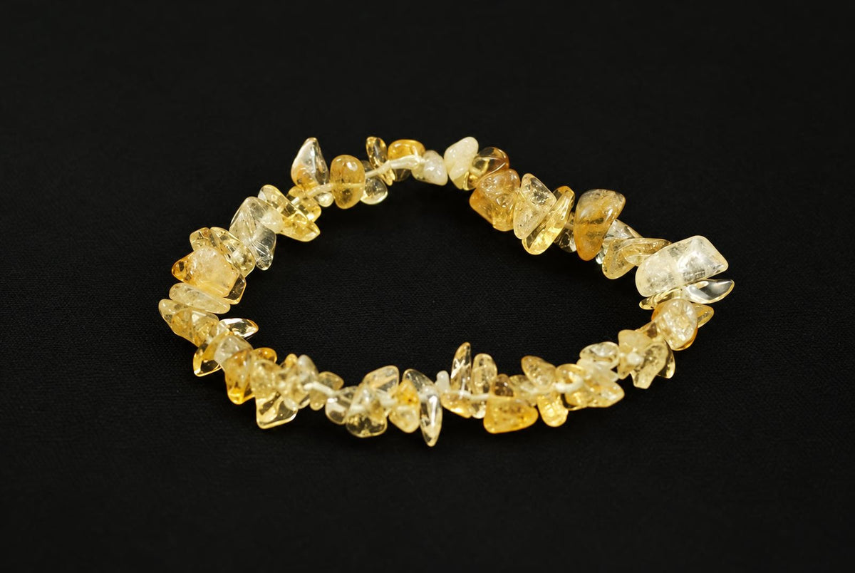 A bracelet made of irregular citrine chips in yellow and pale tones, strung together on a dark surface.