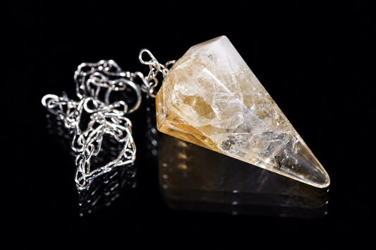 A silver-toned chain holds a large, clear-to-yellow citrine pendulum shaped like a rough crystal point on a dark surface.