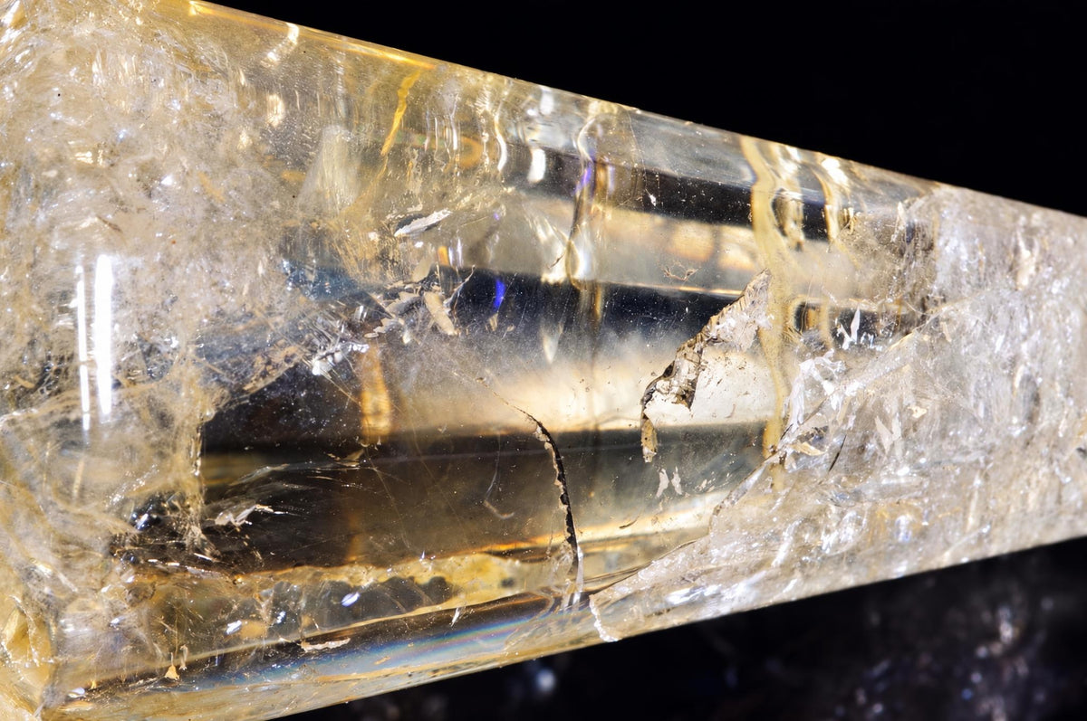 A close-up of a yellow citrine pendulum point with visible internal fractures and inclusions against a dark background.