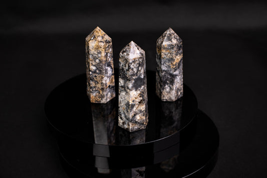 Three polished, faceted agate points with dark and golden-brown patterns stand on a glossy black circular surface.