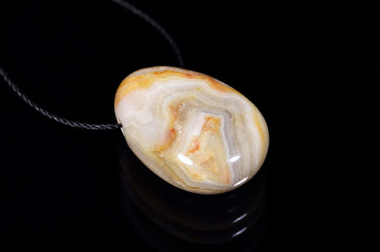 A polished oval pendant with white, cream and orange-brown banding on a dark surface.