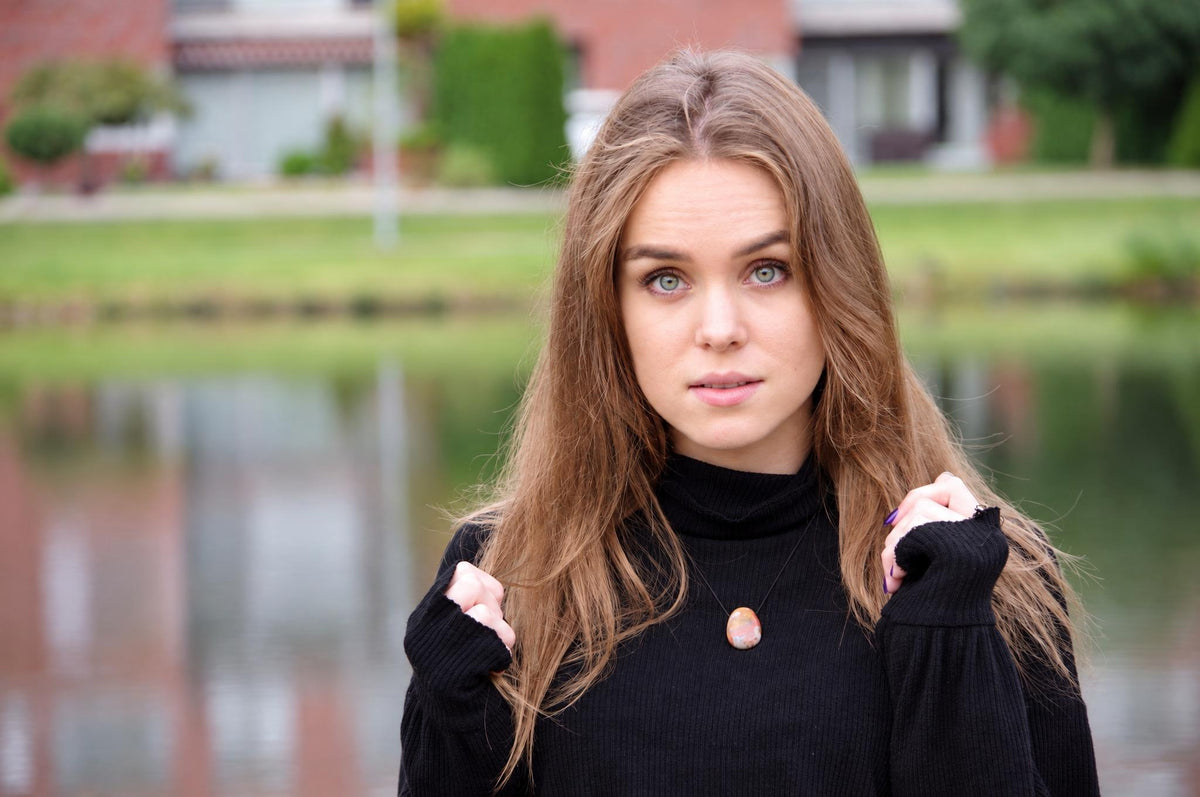 A woman wears a black turtleneck with a pendant featuring an oval, multicoloured stone on a thin cord.