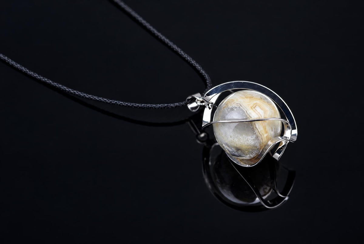 A silver-toned wire pendant holds a round, banded agate stone on a black cord against a dark surface.