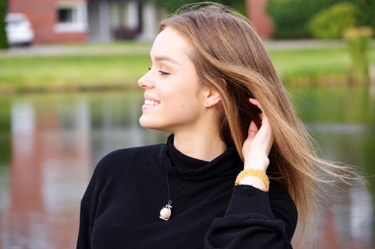 A woman wears a black turtleneck with a silver-toned pendant featuring a pale sphere on a dark surface.