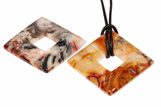 Two square donut-shaped pendants with swirled red, black and cream patterns; one has a black cord looped through its center.