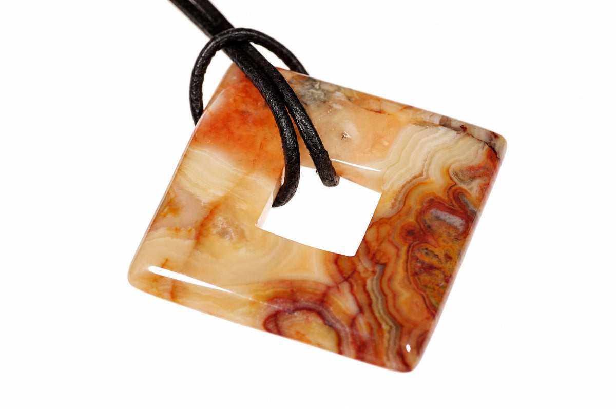 A square, donut-shaped pendant made of polished agate with swirling orange, cream and brown patterns, threaded on a black cord against a white background.