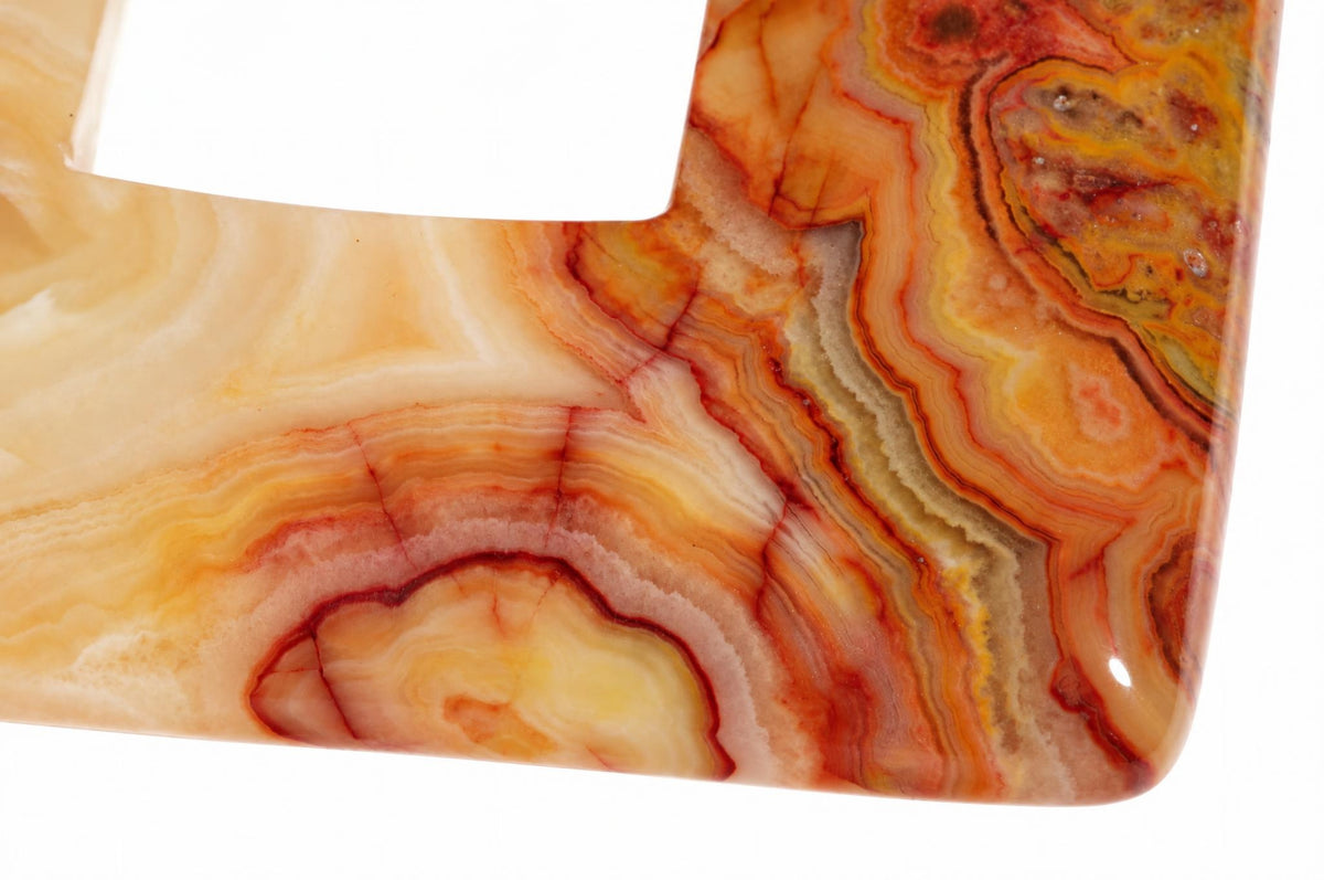 A close-up of a square-shaped pendant with polished crazy lace agate, showing swirling bands of cream, orange, red and brown on a white background.