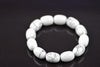 Howlite bracelet with rounded white beads and grey veining arranged in a ring on a dark reflective surface, viewed at an angle with the front beads in focus.