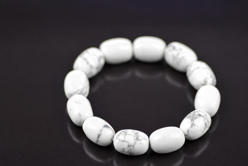 Howlite bracelet with rounded white beads and grey veining arranged in a ring on a dark reflective surface, viewed at an angle with the front beads in focus.