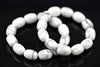 White oval howlite beads with grey veining arranged in overlapping bracelet loops on a dark reflective surface, viewed at an angle with softly blurred rear beads.