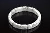 Howlite bracelet with white square beads and grey veining, arranged in a ring on a dark reflective surface, viewed at an angle.