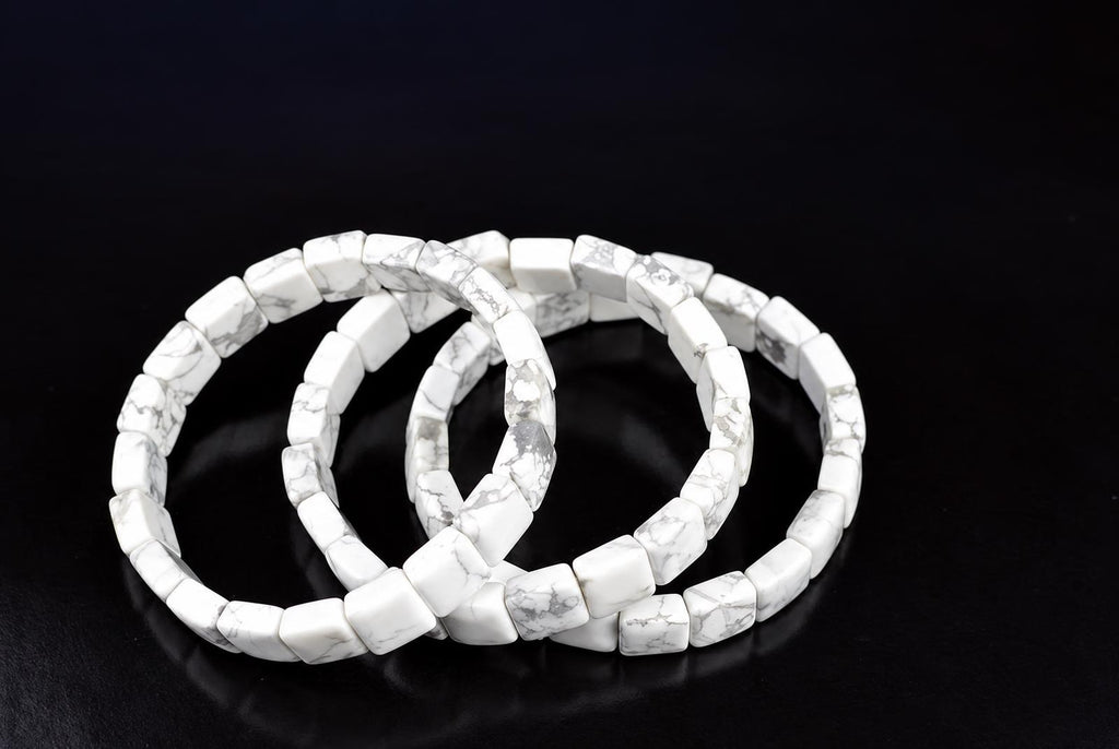Three overlapping bracelets of white square beads with grey veining, arranged on a dark reflective surface.