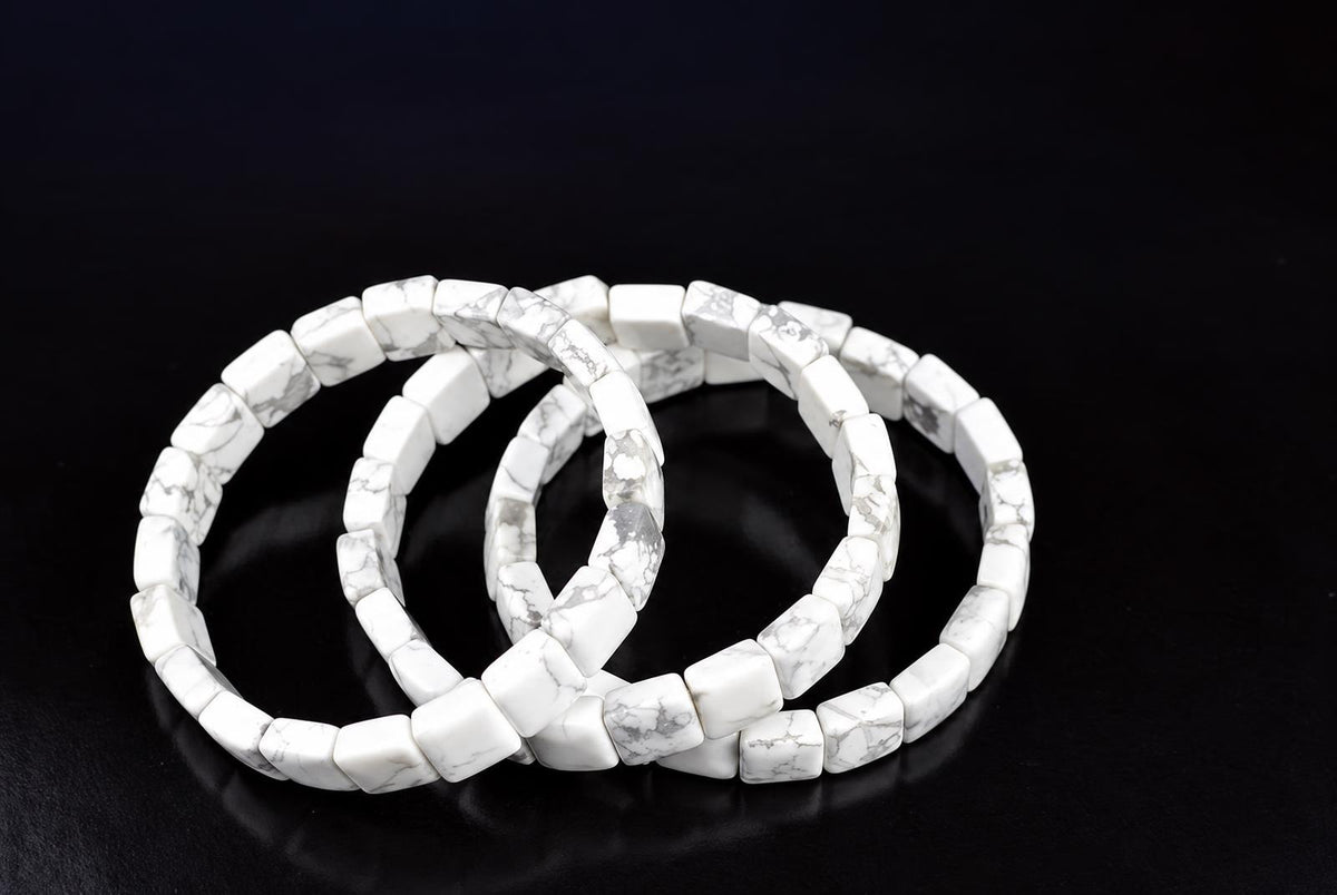 Three overlapping bracelets of white square beads with grey veining, arranged on a dark reflective surface.