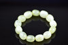 Pale green bracelet with polished oval beads and cloudy white markings, arranged in a circle on a dark reflective surface, viewed from above at an angle.