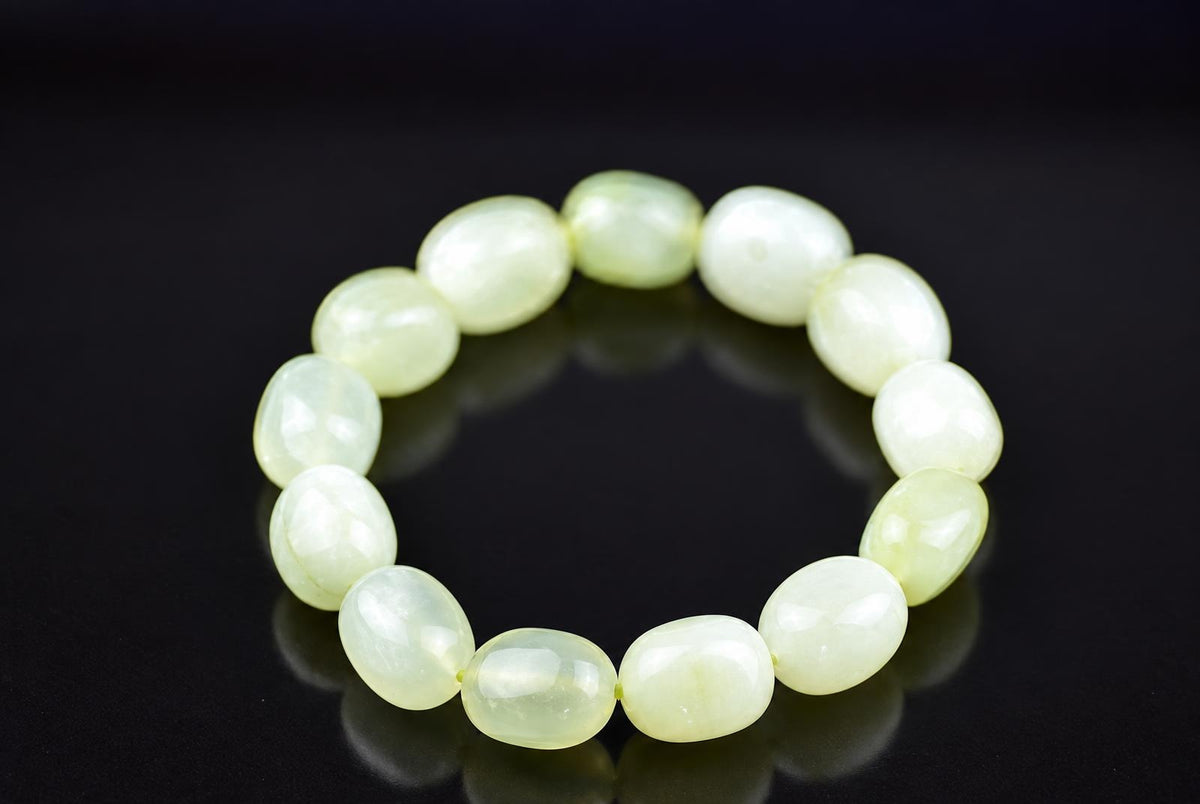 Pale green bracelet with polished oval beads and cloudy white markings, arranged in a circle on a dark reflective surface, viewed from above at an angle.