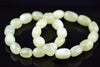 Overlapping loops of polished oval beads in pale green and creamy white, viewed at an angle on a glossy black surface with soft reflections.