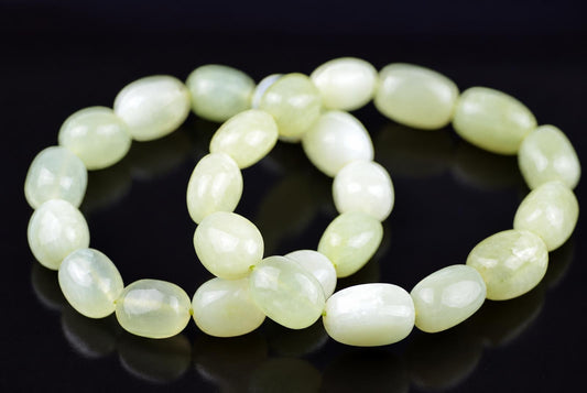 Overlapping loops of polished oval beads in pale green and creamy white, viewed at an angle on a glossy black surface with soft reflections.