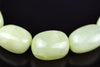 Close-up of polished pale green bracelet beads on a dark background, with a rounded rectangular bead between two oval beads and bright reflections on their surfaces.