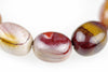 Close-up of rounded bracelet beads with cream, burgundy and mustard-yellow patches and curved bands, arranged in an arc on a white background.