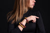 Glossy rounded-bead bracelets in mustard yellow, burgundy, pink and cream worn on a raised wrist, with black clothing and a dark background.
