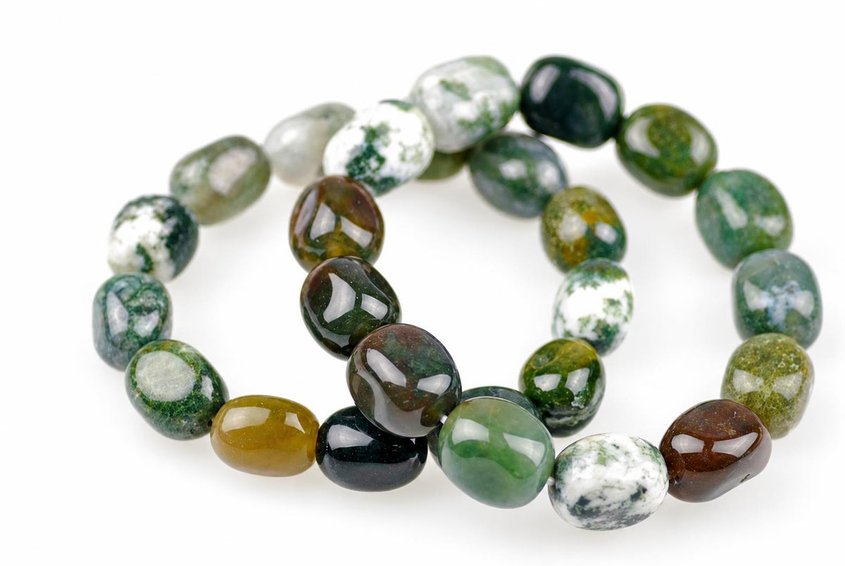 Overlapping loops of glossy, rounded beads in green, white, brown and mustard yellow, with mottled markings, on a white background viewed at an angle.