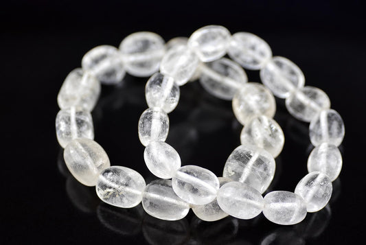 Quartz bead bracelet arranged in overlapping loops on a glossy black surface, with rounded oval, clear-to-cloudy white beads and visible threading.