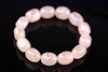 Rose quartz bracelet with pale pink oval beads arranged in a circle on a glossy black surface, with reflections below and softly blurred beads toward the back.