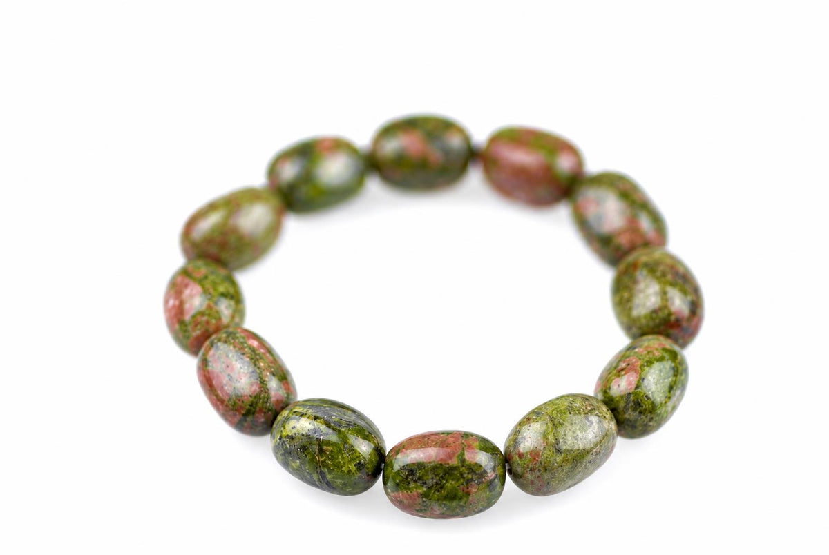 Unakite bracelet with polished oval beads mottled green and pink, arranged in a circle on a white surface, with the front beads in focus and the rear beads softly blurred.