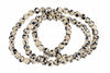 A strand of round beads with a cream base and black spots, arranged in loops on a white background.