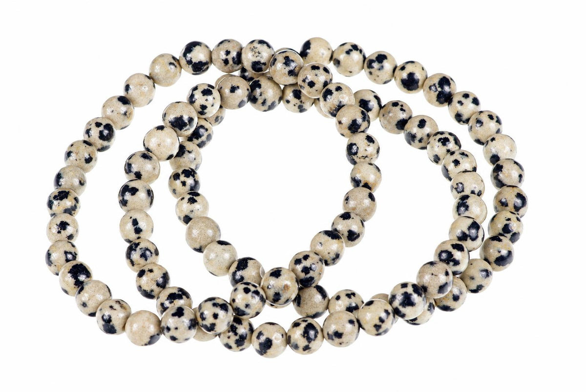 A strand of round beads with a cream base and black spots, arranged in loops on a white background.