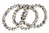 A bracelet of round beads with a cream base and black spots, arranged in loops on a white background.