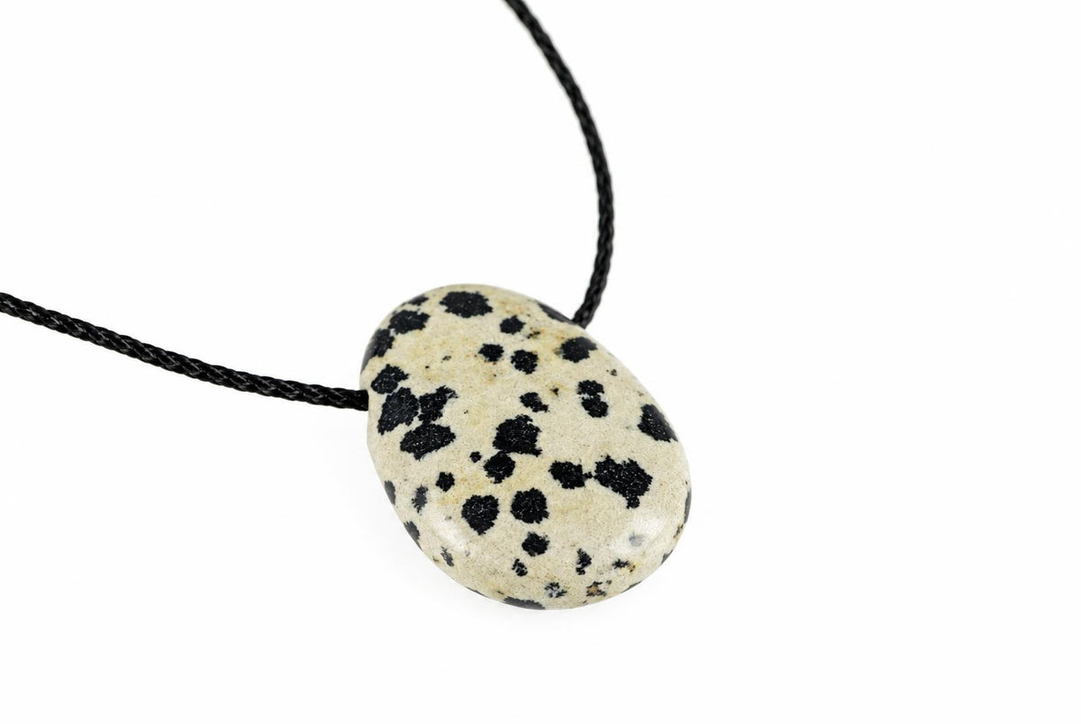 A pendant with a cream-coloured, oval stone featuring black spots, hanging from a dark cord against a white background.
