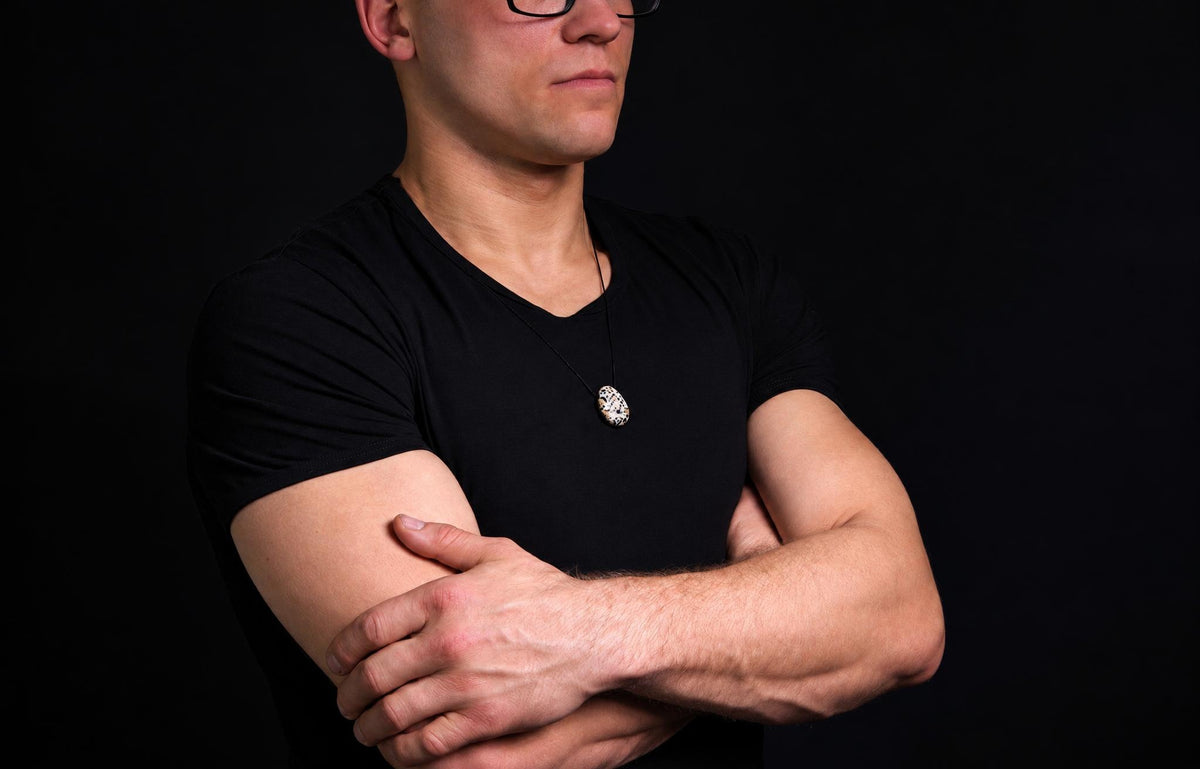 A man in a black t-shirt wears a pendant with a white and black spotted stone on a dark surface.