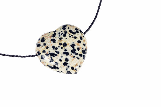 A heart-shaped pendant with a cream background and black spots, resembling Dalmatian jasper, on a dark cord against a white surface.