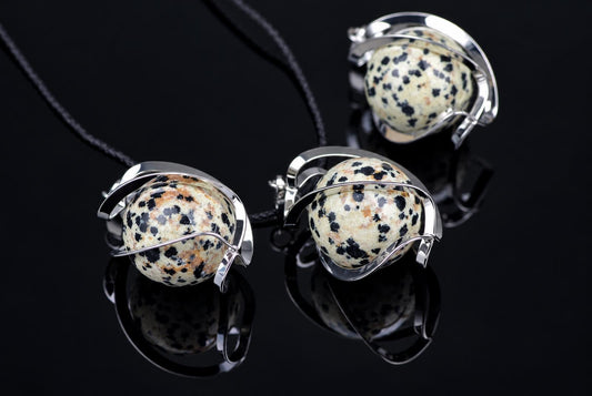 Three silver-toned pendants with spotted spheres on black cords, arranged on a dark reflective surface.
